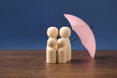 Photo of Human figures under umbrella on wooden table against blue background. Insurance concept