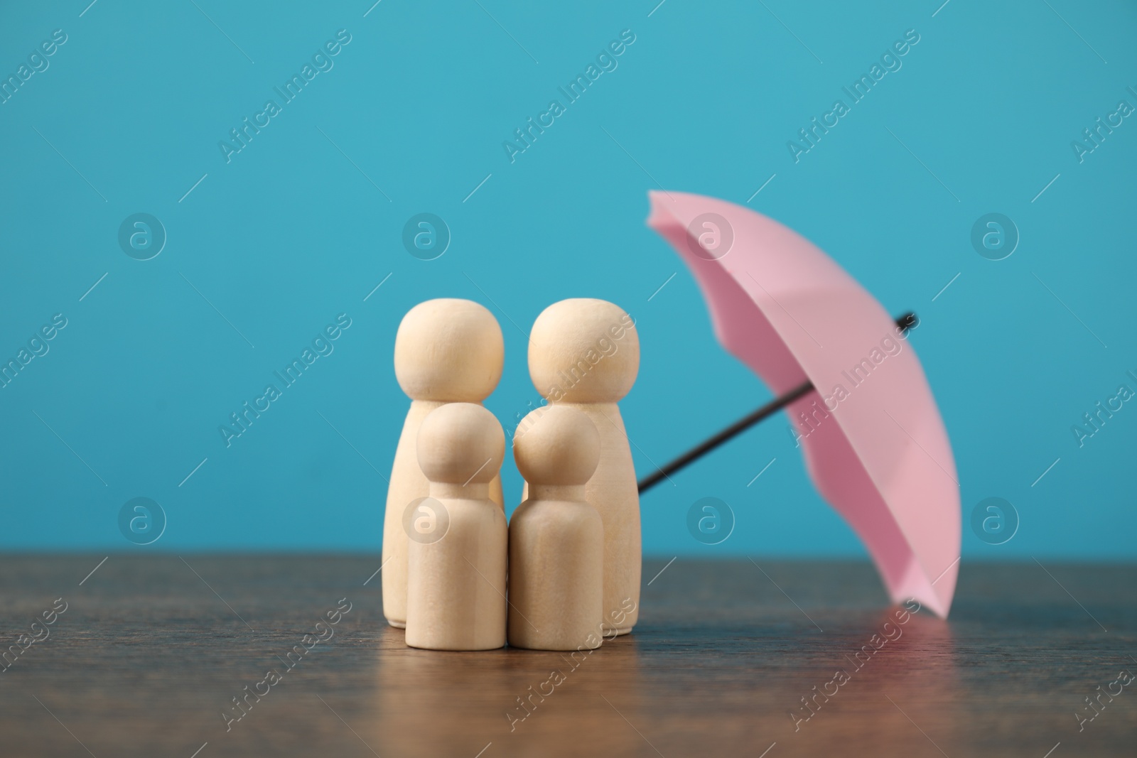 Photo of Human figures under umbrella on wooden table against light blue background. Insurance concept