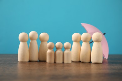 Photo of Human figures with umbrella on wooden table against light blue background. Insurance concept