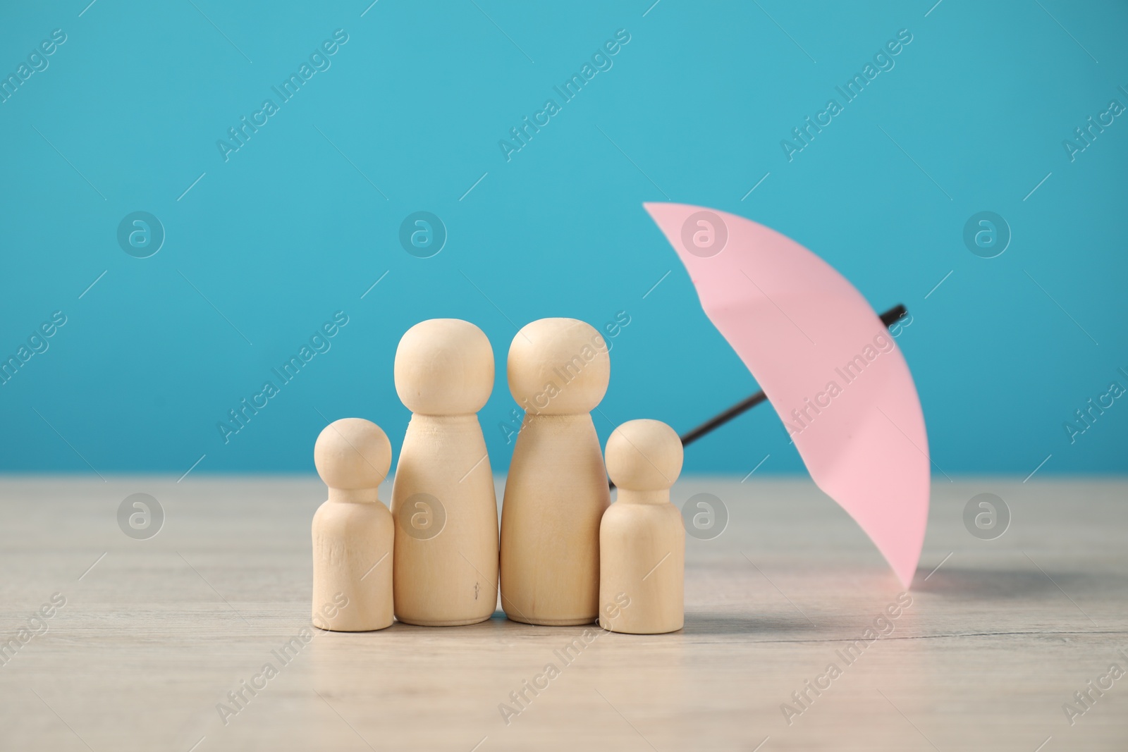 Photo of Human figures under umbrella on wooden table against light blue background. Insurance concept