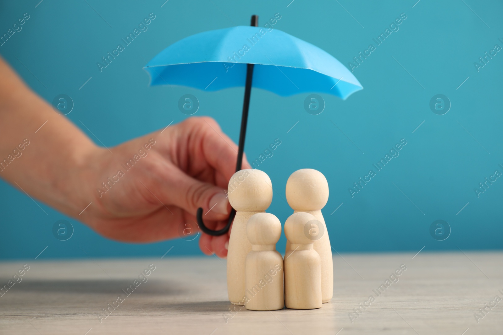 Photo of Woman holding umbrella over human figures at light wooden table, closeup. Insurance concept