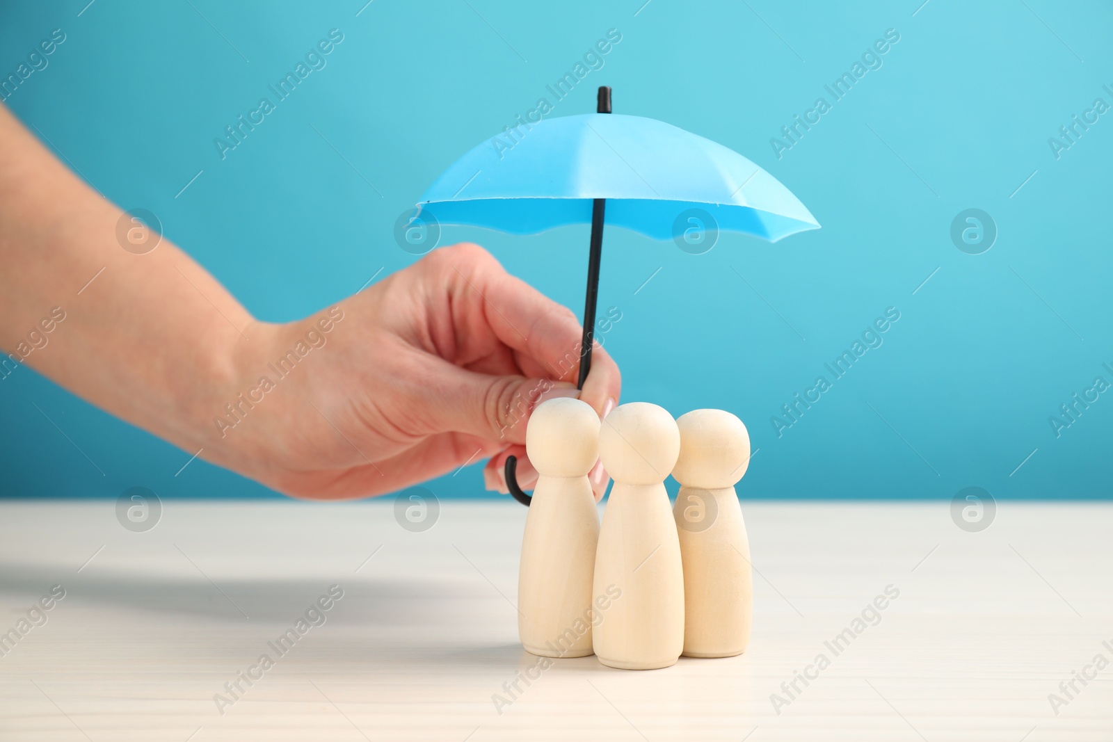 Photo of Woman holding umbrella over human figures at white table, closeup. Insurance concept