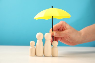 Photo of Woman holding umbrella over human figures at white table, closeup. Insurance concept