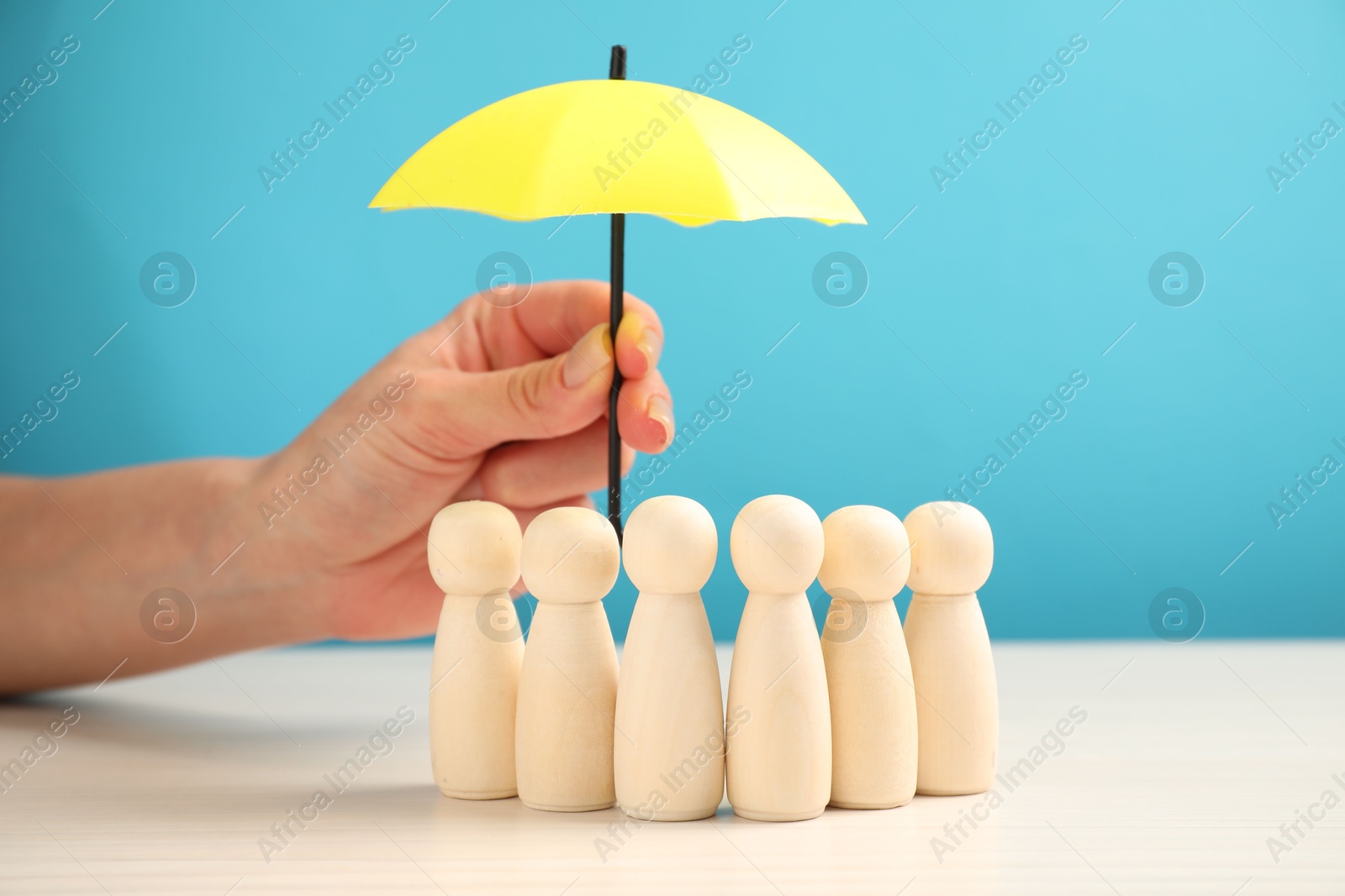 Photo of Woman holding umbrella over human figures at white table, closeup. Insurance concept