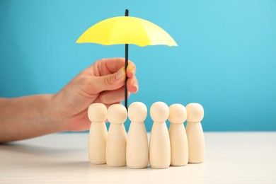 Photo of Woman holding umbrella over human figures at white table, closeup. Insurance concept