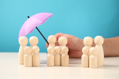 Photo of Woman holding umbrella over human figures at white table, closeup. Insurance concept