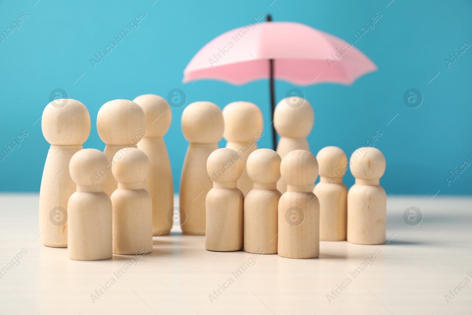 Photo of Human figures under umbrella on white table against light blue background. Insurance concept