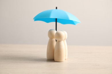 Photo of Human figures under umbrella on light wooden table. Insurance concept