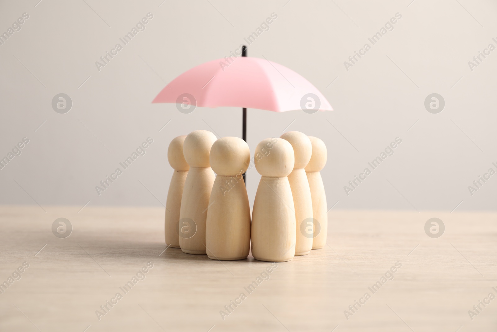 Photo of Human figures under umbrella on light wooden table. Insurance concept