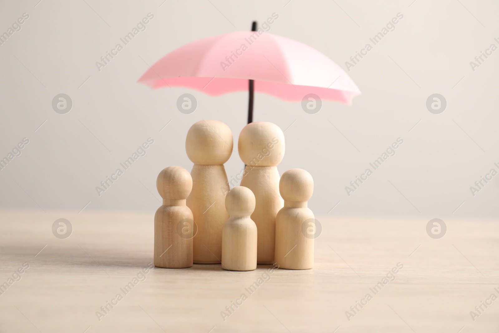 Photo of Human figures under umbrella on light wooden table. Insurance concept