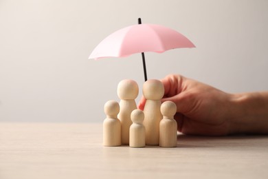 Photo of Woman holding umbrella over human figures at light wooden table, closeup. Insurance concept