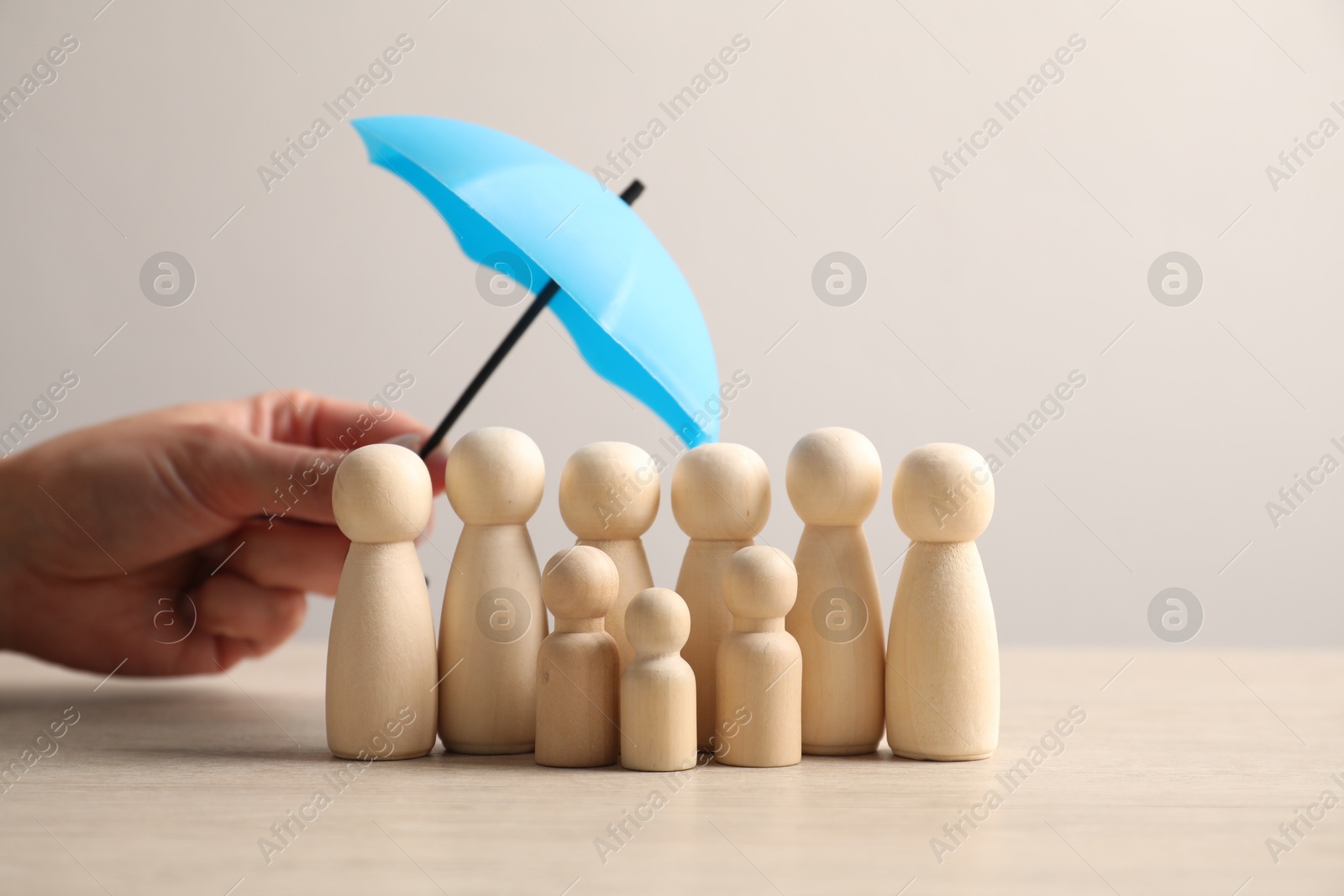 Photo of Woman holding umbrella over human figures at light wooden table, closeup. Insurance concept