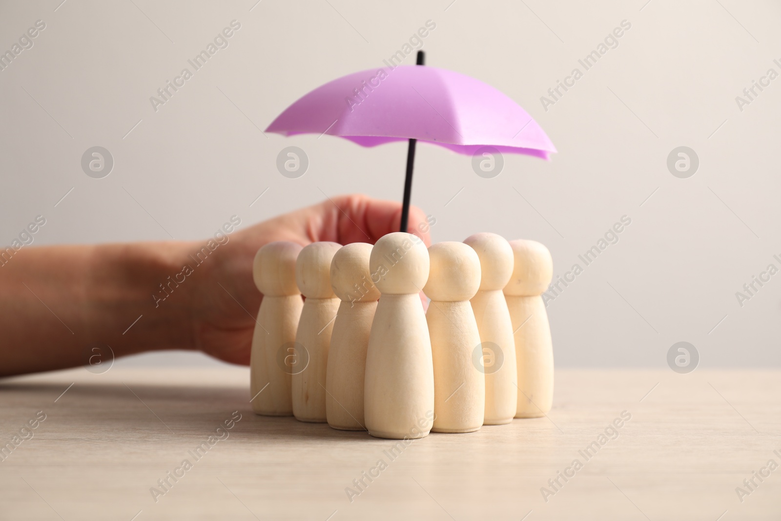 Photo of Woman holding umbrella over human figures at light wooden table, closeup. Insurance concept