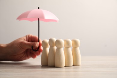 Photo of Woman holding umbrella over human figures at light wooden table, closeup. Insurance concept