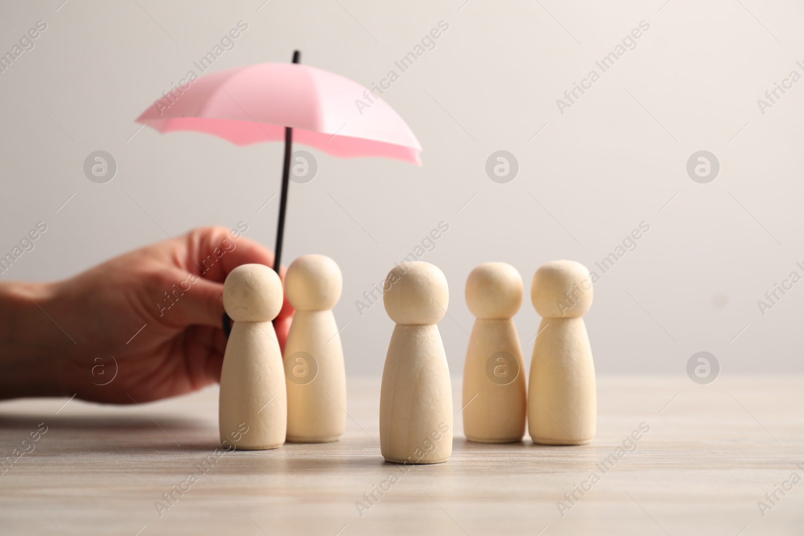 Photo of Woman holding umbrella over human figures at light wooden table, closeup. Insurance concept