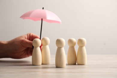 Photo of Woman holding umbrella over human figures at light wooden table, closeup. Insurance concept