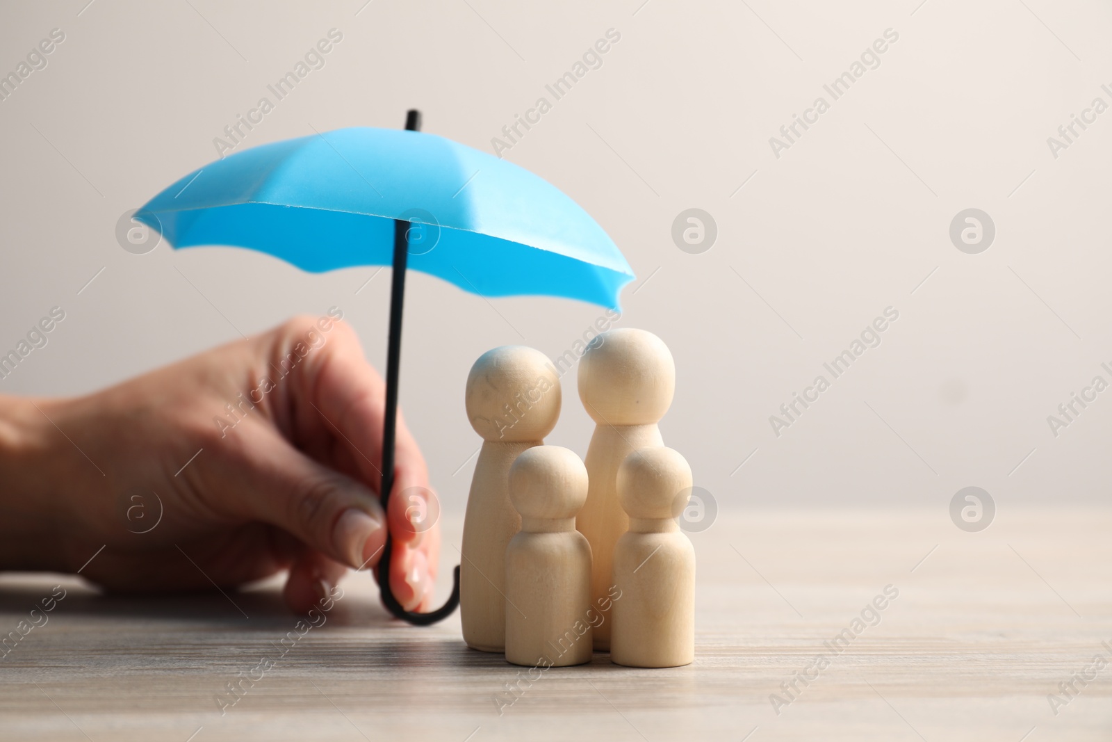 Photo of Woman holding umbrella over human figures at light wooden table, closeup. Insurance concept