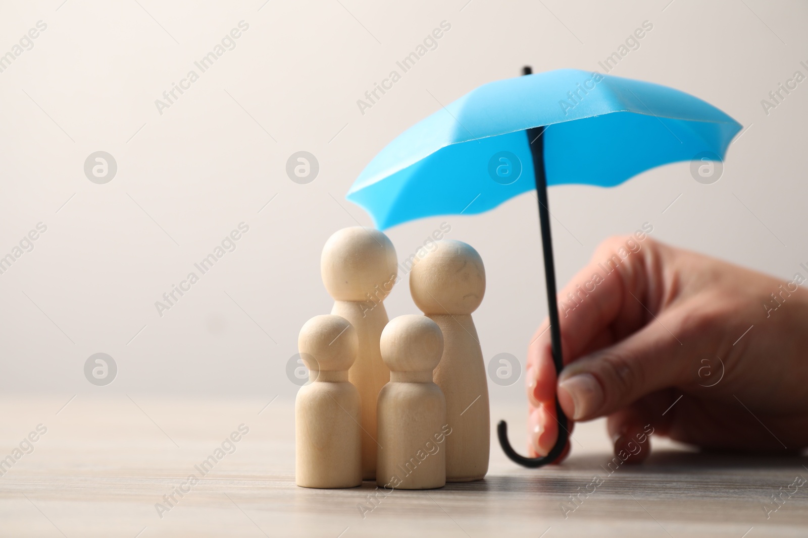 Photo of Woman holding umbrella over human figures at light wooden table, closeup. Insurance concept