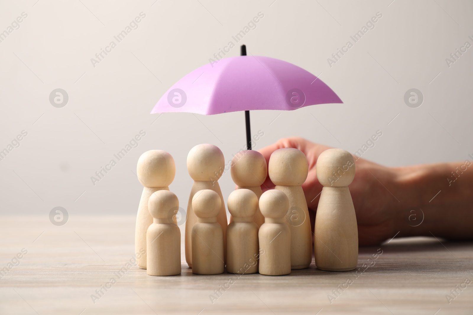 Photo of Woman holding umbrella over human figures at light wooden table, closeup. Insurance concept