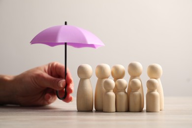 Photo of Woman holding umbrella over human figures at light wooden table, closeup. Insurance concept