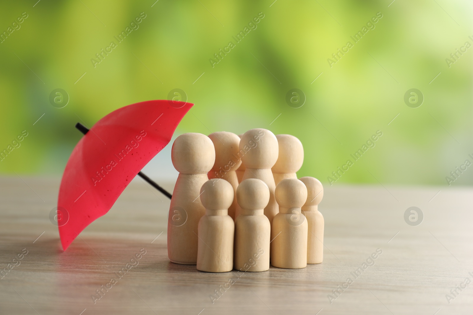 Photo of Human figures under umbrella on light wooden table outdoors. Insurance concept