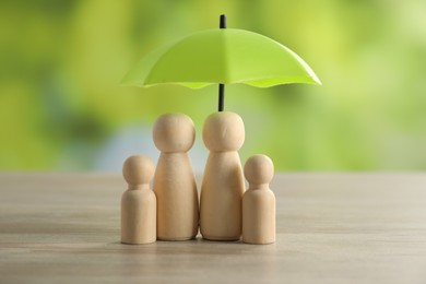 Photo of Human figures under umbrella on light wooden table outdoors. Insurance concept