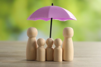 Photo of Human figures under umbrella on light wooden table outdoors. Insurance concept