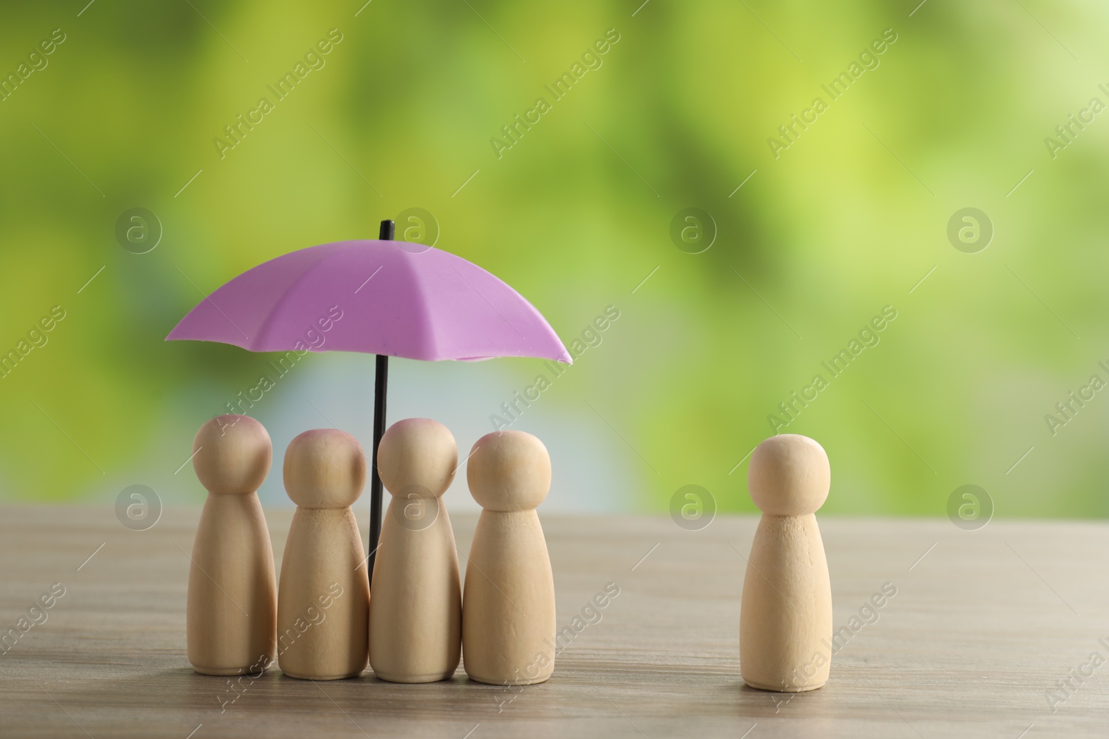 Photo of Human figures under umbrella and wooden one on table outdoors. Insurance concept