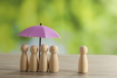 Photo of Human figures under umbrella and wooden one on table outdoors. Insurance concept