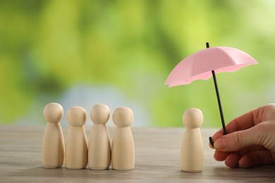 Photo of Woman holding umbrella over human figure at wooden table outdoors, closeup. Insurance concept