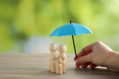 Photo of Woman holding umbrella over human figures at wooden table outdoors, closeup. Insurance concept