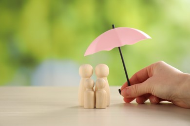 Photo of Woman holding umbrella over human figures at light wooden table outdoors, closeup. Insurance concept