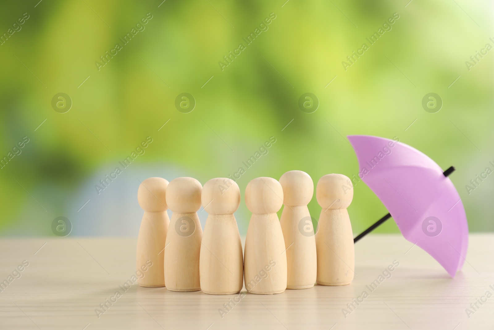 Photo of Human figures under umbrella on light wooden table outdoors. Insurance concept