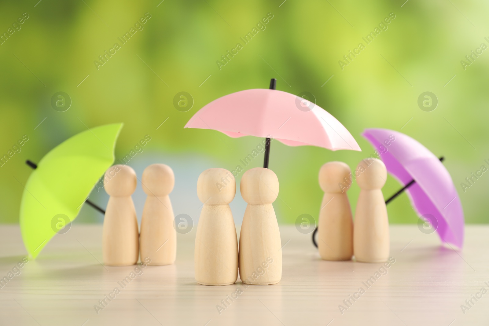 Photo of Human figures under umbrellas on light wooden table outdoors. Insurance concept