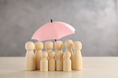 Photo of Human figures under umbrella on light wooden table. Insurance concept