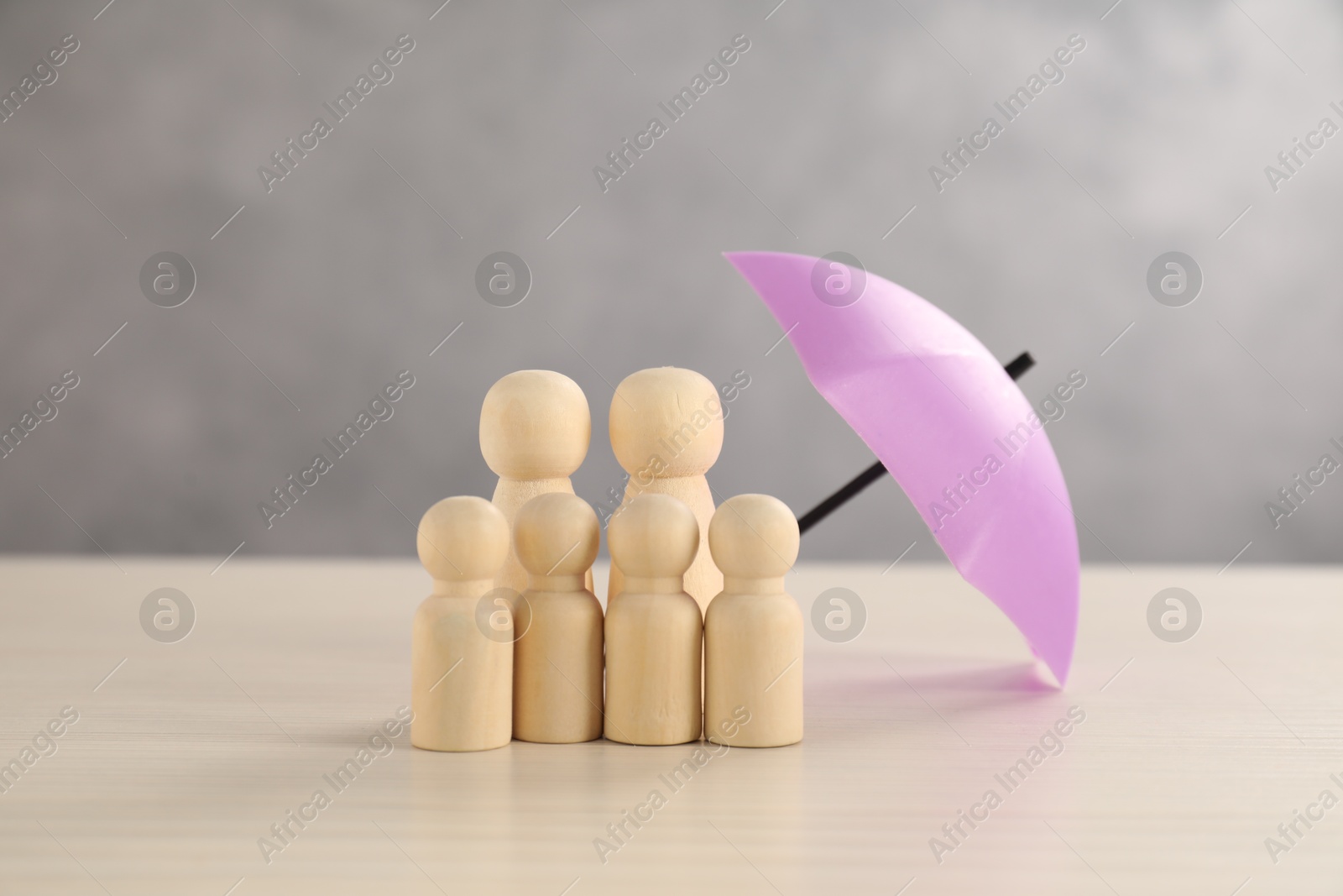 Photo of Human figures under umbrella on light wooden table. Insurance concept