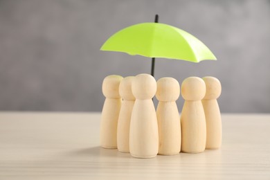 Photo of Human figures under umbrella on light wooden table. Insurance concept