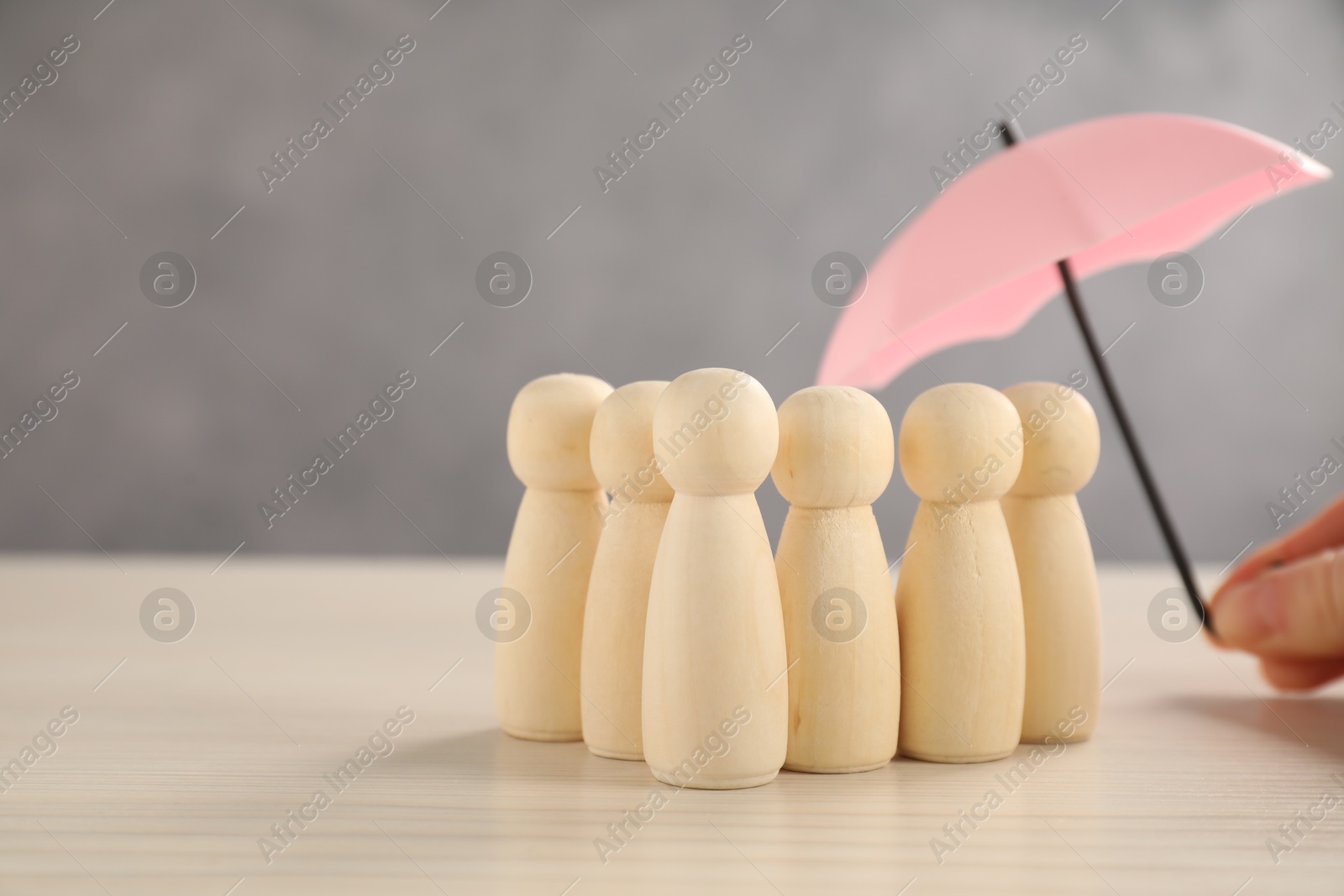 Photo of Woman holding umbrella over human figures at light wooden table, closeup. Insurance concept