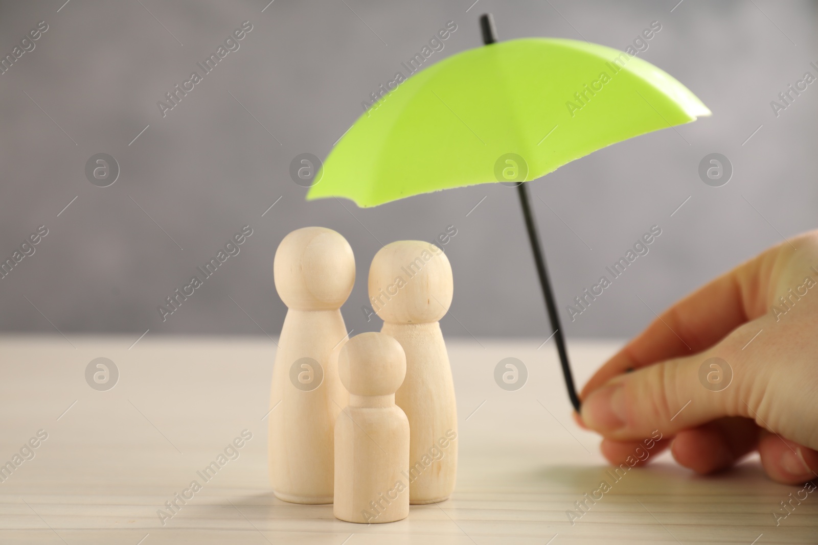 Photo of Woman holding umbrella over human figures at light wooden table, closeup. Insurance concept