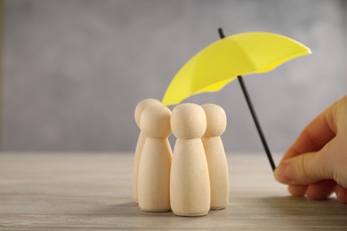 Photo of Woman holding umbrella over human figures at wooden table, closeup. Insurance concept