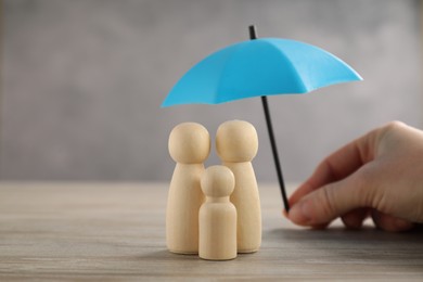 Photo of Woman holding umbrella over human figures at wooden table, closeup. Insurance concept