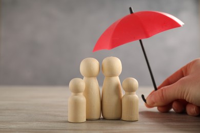 Photo of Woman holding umbrella over human figures at wooden table, closeup. Insurance concept