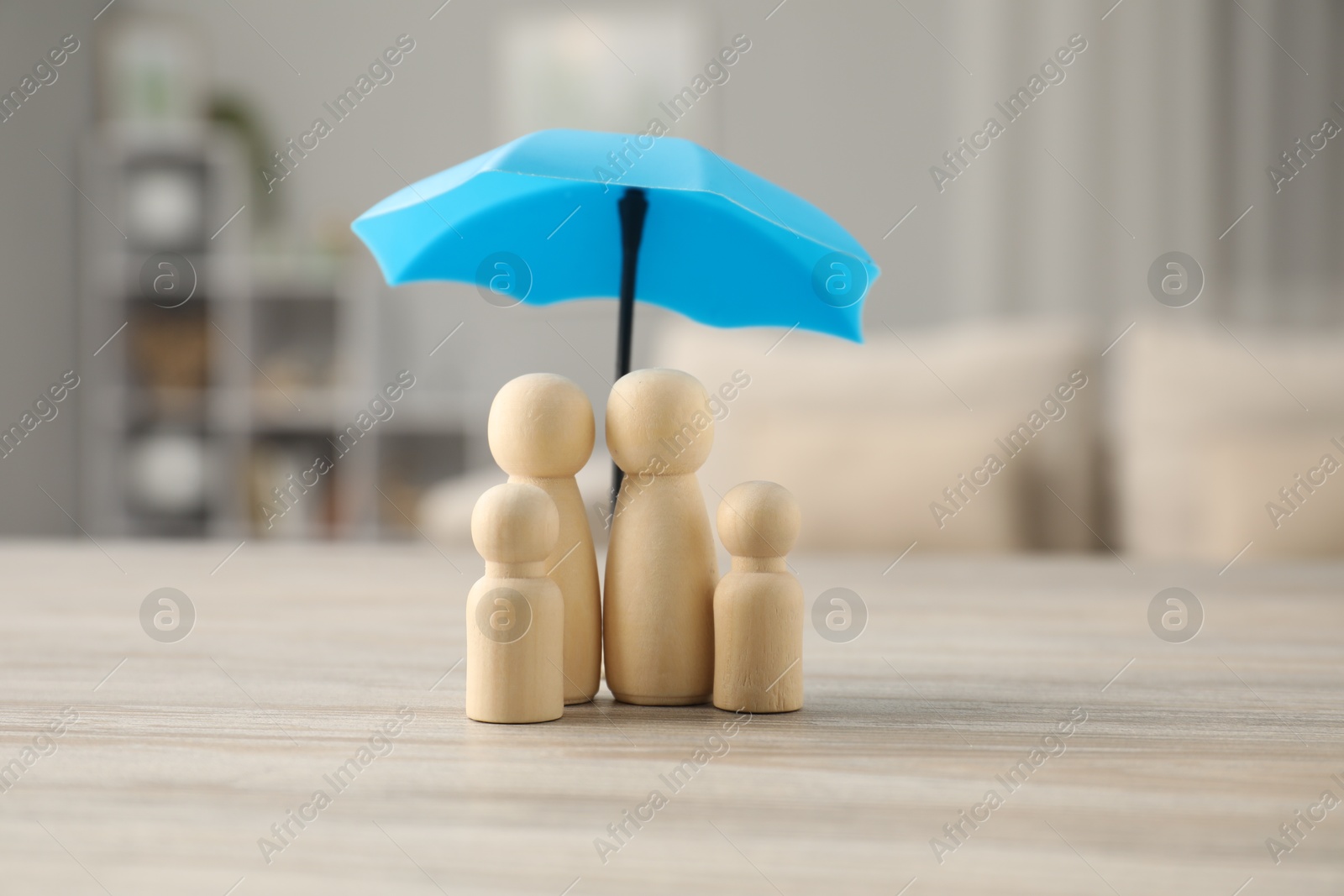 Photo of Human figures under umbrella on light wooden table indoors. Insurance concept