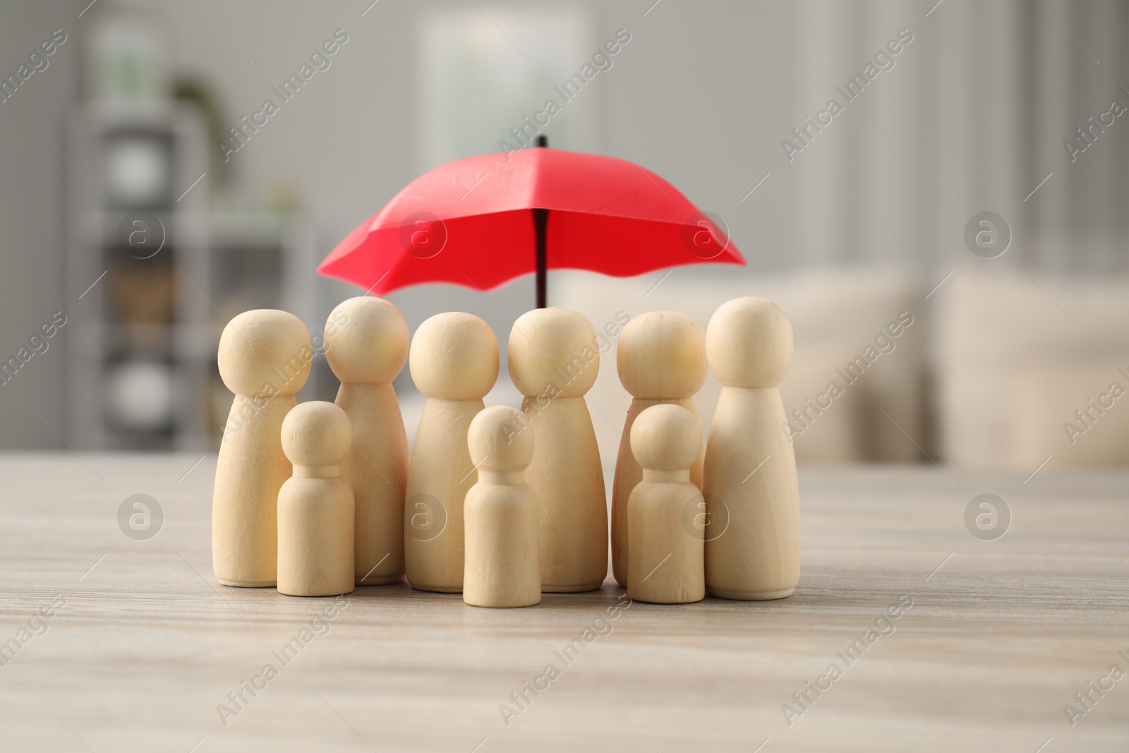 Photo of Human figures under umbrella on light wooden table indoors. Insurance concept