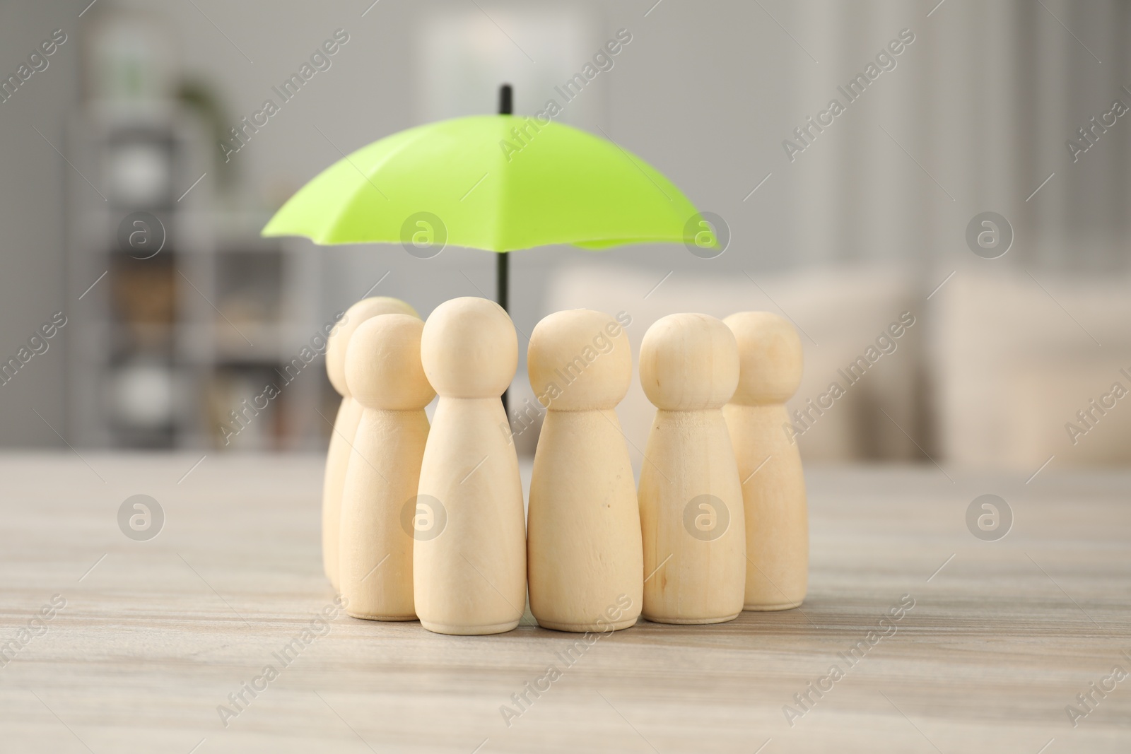 Photo of Human figures under umbrella on light wooden table indoors. Insurance concept