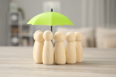 Photo of Human figures under umbrella on light wooden table indoors. Insurance concept