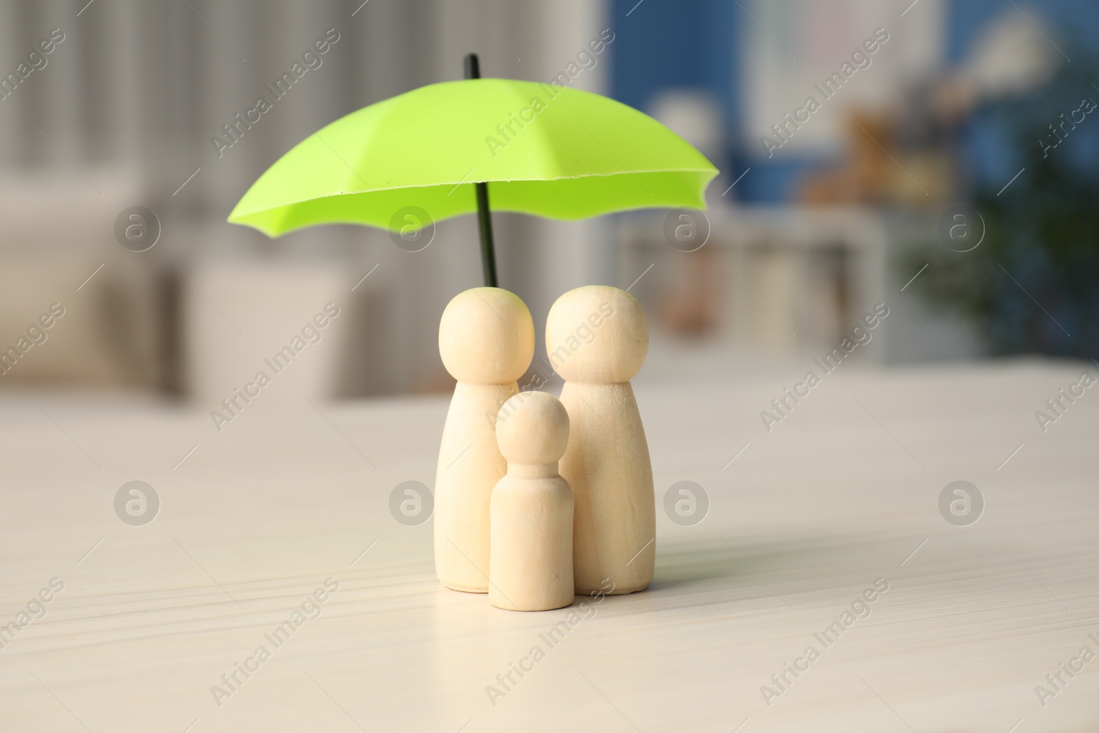 Photo of Human figures under umbrella on white wooden table indoors. Insurance concept