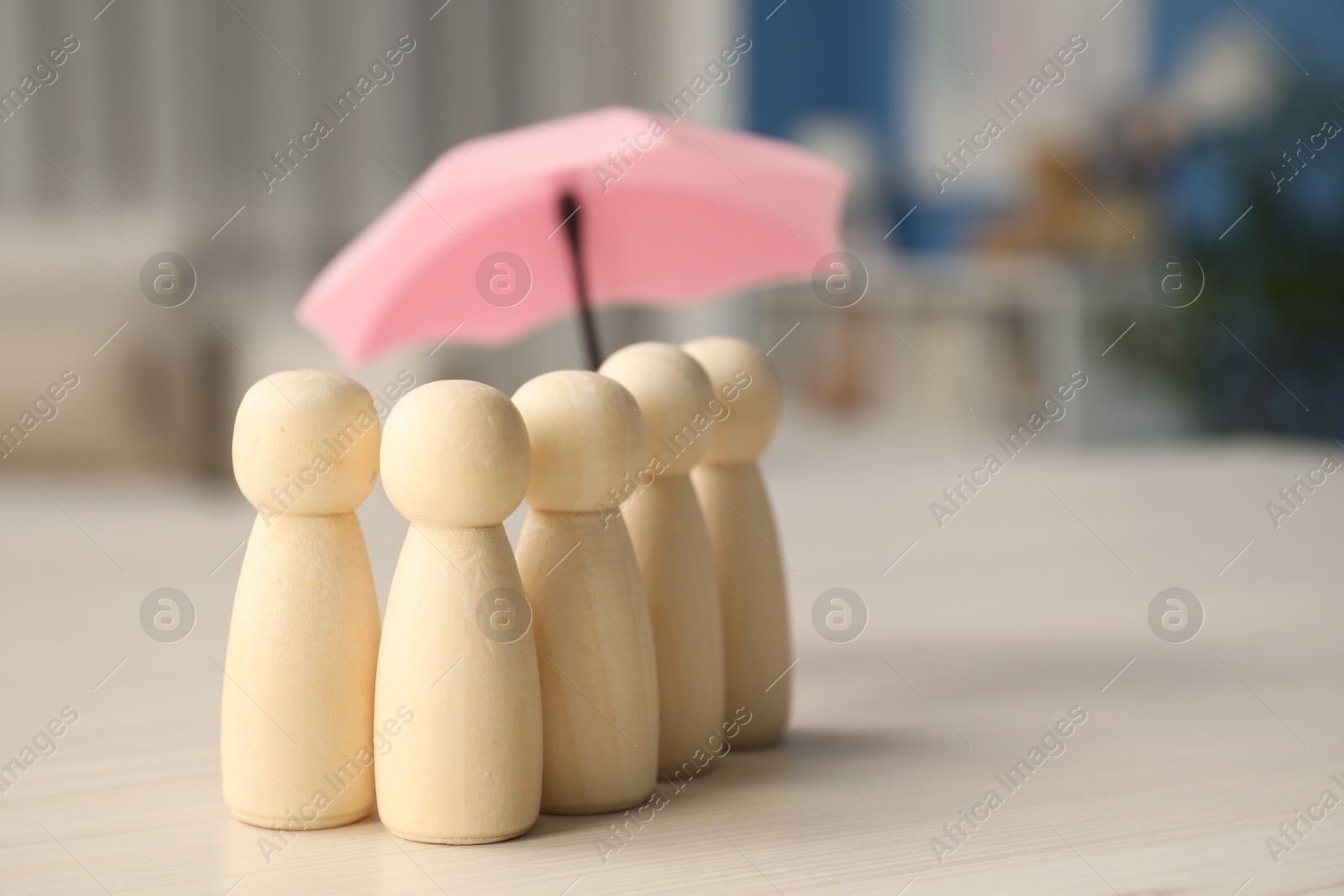 Photo of Insurance concept. Human figures under umbrella on white wooden table, closeup. Space for text