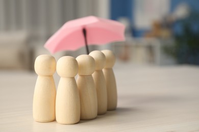 Photo of Insurance concept. Human figures under umbrella on white wooden table, closeup. Space for text