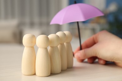 Photo of Woman holding umbrella over human figures at white wooden table indoors, closeup. Insurance concept